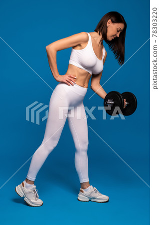 Woman one arm bicep curl with dumbbell on blue background Woman one arm bicep curl with dumbbell on blue background 78303220