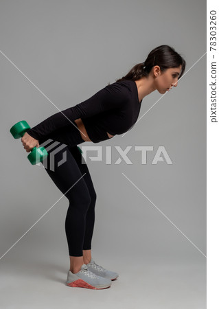 Sporty girl performing triceps kickback with dumbbells on grey background Sporty girl performing triceps kickback with dumbbells on grey background 78303260