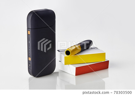 New generation black electronic cigarette is on packs with red and yellow sides, battery, isolated on white. Heating tobacco system. Close up New generation black electronic cigarette is on packs with red and yellow sides, battery, isolated on white. Heating tobacco system. Close up 78303500