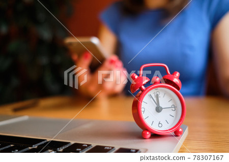A girl dressed in a blue dress works in a smartphone in the foreground a red clock. Concept dead line. 78307167