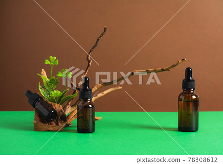 Serum and oil cosmetic bottles with wooden branch and green plants on brown and green background Serum and oil cosmetic bottles with wooden branch and green plants on brown and green background 78308612