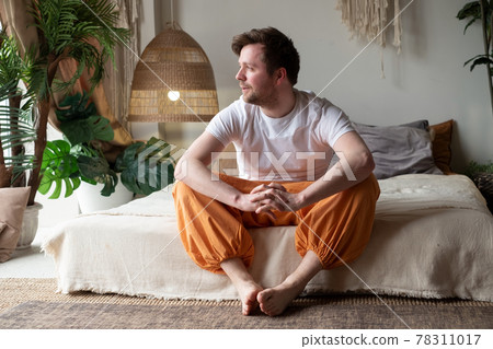 Smiling young man sitting on his bed while looking at the camera 78311017