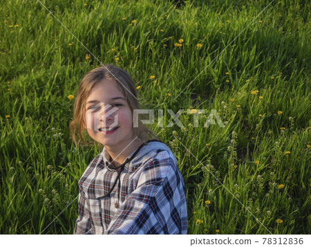Smiling teenage girl on a walk in the park sits on a blooming green meadow in the sun. Smiling teenage girl on a walk in the park sits on a blooming green meadow in the sun. 78312836