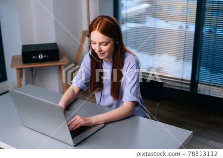 Top view of attractive young woman operator using headset and laptop during customer support at home office. 78313112