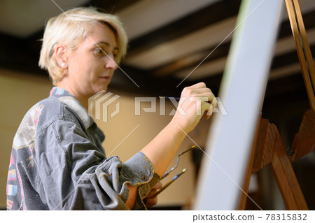 Female creative artist painter concentrated and inspired painting picture with paint brush and oil Female creative artist painter concentrated and inspired painting picture with paint brush and oil 78315832
