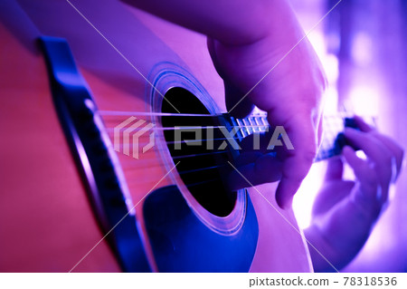 Male hands playing fingers style on a western dreadnought guitar in purple neon light. Male hands playing fingers style on a western dreadnought guitar in purple neon light. 78318536