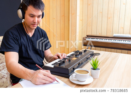 asian handsome male songwriter enjoy writing a hit song while playing music keyboard in living room. songwriting concept asian handsome male songwriter enjoy writing a hit song while playing music keyboard in living room. songwriting concept 78318685