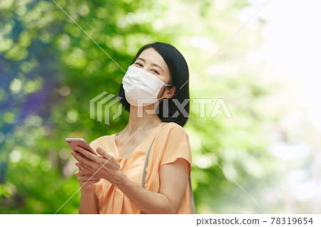 A middle-aged woman wearing a mask in the fresh green and holding a smartphone A middle-aged woman wearing a mask in the fresh green and holding a smartphone 78319654