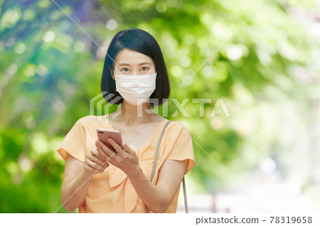 A middle-aged woman wearing a mask in the fresh green and holding a smartphone A middle-aged woman wearing a mask in the fresh green and holding a smartphone 78319658