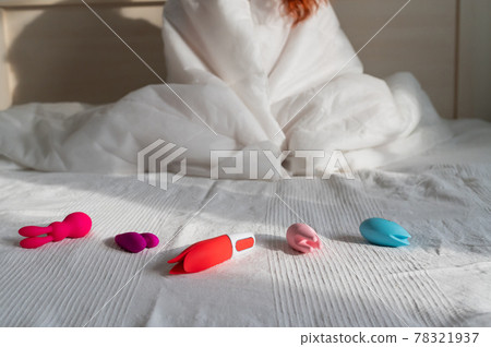 Woman sitting on bed next to a collection of vibrators and sex toys 78321937