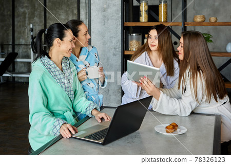 Family is discussing something at breakfast using electronic devices, women are conferring sitting at table in dressing gowns. Family is discussing something at breakfast using electronic devices, women are conferring sitting at table in dressing gowns. 78326123