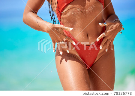 Close-up tanned parts of female body on the beach in a red bikini Close-up tanned parts of female body on the beach in a red bikini 78326778