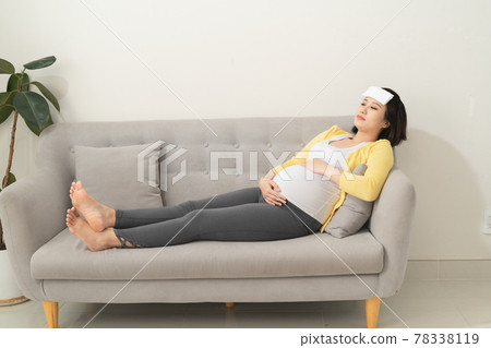 Young pregnant woman having a headache and she is lying on the sofa Young pregnant woman having a headache and she is lying on the sofa 78338119