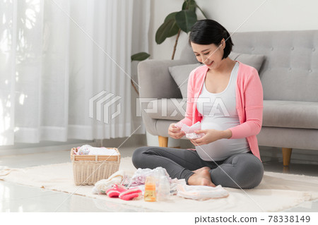 beautiful pregnant asian woman using pen writing list on notebook packing and preparing baby clothes in basket beautiful pregnant asian woman using pen writing list on notebook packing and preparing baby clothes in basket 78338149