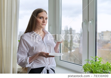 Beautiful young woman with blond long hair holding cup coffee near window 78338400