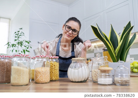 Storing food in kitchen, woman with jars and containers talking and looking at camera 78338620