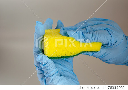 A hand in a blue protective glove holds a new sponge. A hand in a blue protective glove holds a new sponge. 78339031