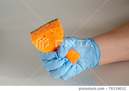 A hand in a blue protective glove holds a new sponge. A hand in a blue protective glove holds a new sponge. 78339032