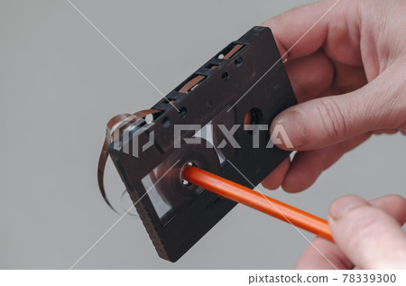 Close-up of a male hand with an old audio cassette and a pencil. 78339300