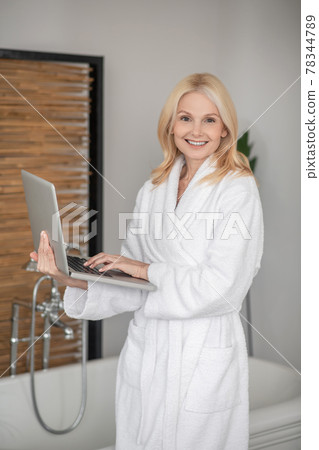 Beautiful blonde woman in a white bath robe with a laptop 78344789