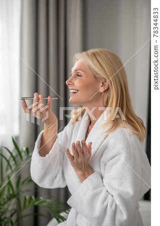 A blonde woman recording a voice message and looking happy 78344833