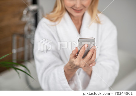 A woman in a white bath robe with a smartphone in her hands A woman in a white bath robe with a smartphone in her hands 78344861