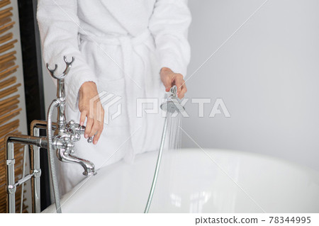 Close up of a woman in a white bath robe holding the shower 78344995