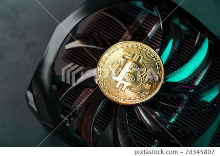 Gold Bitcoin on the video card cooler on a dark background top view. Gold Bitcoin on the video card cooler on a dark background top view. 78345807