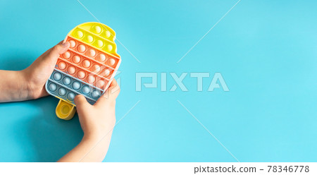 Fashionable touch bright toy antistress pop it in children's hands blue background copy space 78346778