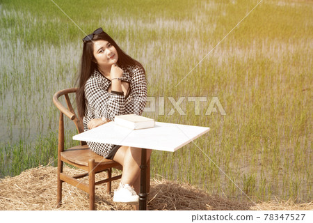 Young pretty Asian fat woman sitting on a table at the rice field. 78347527