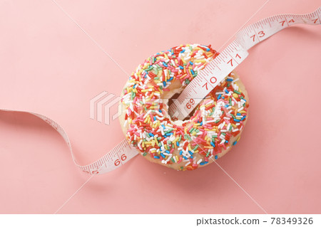 Close up of donuts and measurement tape on pink background. Close up of donuts and measurement tape on pink background. 78349326