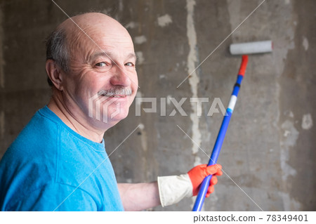 Man painting cement walls using roller brush and primer making a renovation. Man painting cement walls using roller brush and primer making a renovation. 78349401