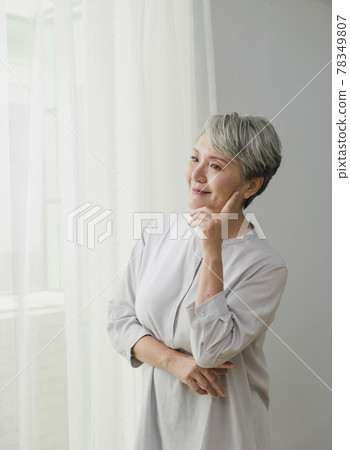 Portrait of an older woman with silver hair by a floor-to-ceiling window 78349807