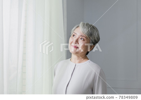 Portrait of an older woman with silver hair by a floor-to-ceiling window Portrait of an older woman with silver hair by a floor-to-ceiling window 78349809