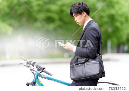 A young man who stops his bicycle and looks at his smartphone 78352212