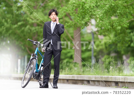 A young man who stops his bicycle and talks on his smartphone 78352220