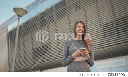 Portrait woman looking at smartphone while running outdoor. Close-up Of A Young Beautiful Sports Fitness Girl Holding A Smartphone In The Hands, Using A Fitness App. Modern City Shooting On the Street 78353690