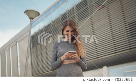 Portrait woman looking at smartphone while running outdoor. Close-up Of A Young Beautiful Sports Fitness Girl Holding A Smartphone In The Hands, Using A Fitness App. Modern City Shooting On the Street 78353698