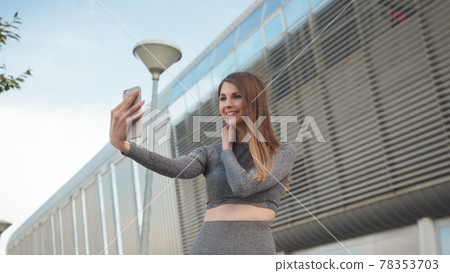 POV of the charming and happy girl. Close-up Of A Beautiful Sports Girl Holding A Smartphone. Close up of the young caucasian woman having a video chat on the modern building background. Outdoors. one POV of the charming and happy girl. Close-up Of A Beautiful Sports Girl Holding A Smartphone. Close up of the young caucasian woman having a video chat on the modern building background. Outdoors. one 78353703