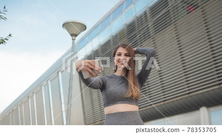 POV of the charming and happy girl. Close-up Of A Beautiful Sports Girl Holding A Smartphone. Close up of the young caucasian woman having a video chat on the modern building background. Outdoors. one POV of the charming and happy girl. Close-up Of A Beautiful Sports Girl Holding A Smartphone. Close up of the young caucasian woman having a video chat on the modern building background. Outdoors. one 78353705