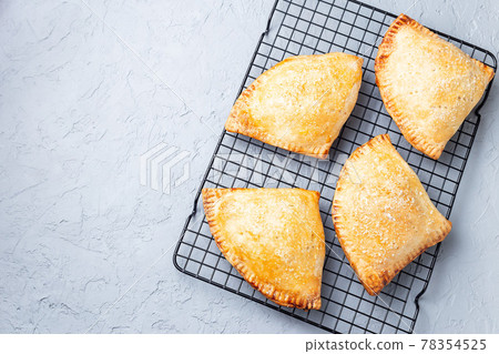 Homemade small peach and cinnamon hand pies with crust dough,  sprinkled with sugar, on cooling rack, top view, horizontal, copy space 78354525