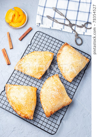 Homemade small peach and cinnamon hand pies with crust dough, sprinkled with sugar, on cooling rack, vertical, top view Homemade small peach and cinnamon hand pies with crust dough, sprinkled with sugar, on cooling rack, vertical, top view 78354527