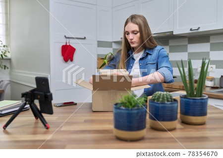 Woman recording video on smartphone unpacking cardboard box. Pet parrot helping to unpack 78354670