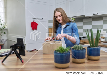 Woman recording video on smartphone unpacking cardboard box. Pet parrot helping to unpack Woman recording video on smartphone unpacking cardboard box. Pet parrot helping to unpack 78354680