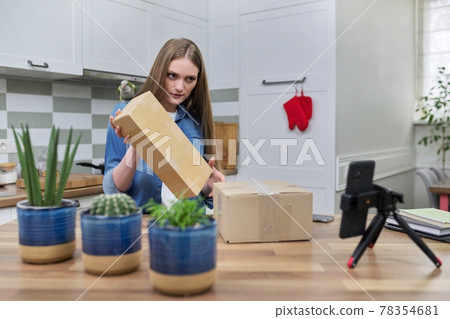 Woman recording video on smartphone unpacking cardboard box. Pet parrot helping to unpack 78354681