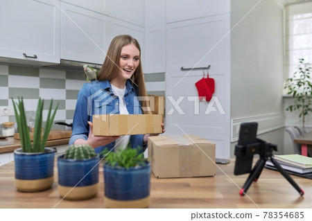 Woman recording video on smartphone unpacking cardboard box. Pet parrot helping to unpack Woman recording video on smartphone unpacking cardboard box. Pet parrot helping to unpack 78354685
