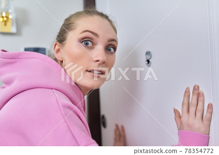 Young woman looking through peephole of front door in apartment. Young woman looking through peephole of front door in apartment. 78354772