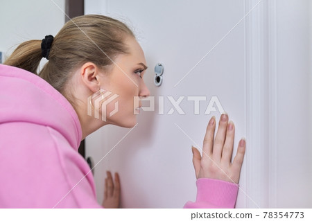 Young woman looking through peephole of front door in apartment. Young woman looking through peephole of front door in apartment. 78354773