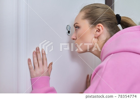 Young woman looking through peephole of front door in apartment. Young woman looking through peephole of front door in apartment. 78354774