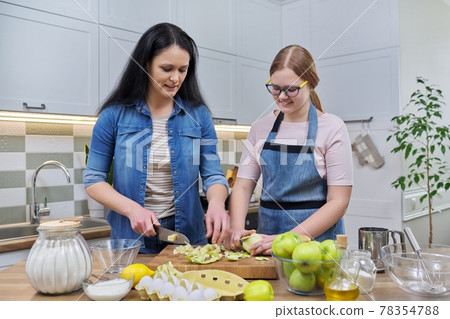 Mom and teen daughter cooking apple pie together at home kitchen Mom and teen daughter cooking apple pie together at home kitchen 78354788